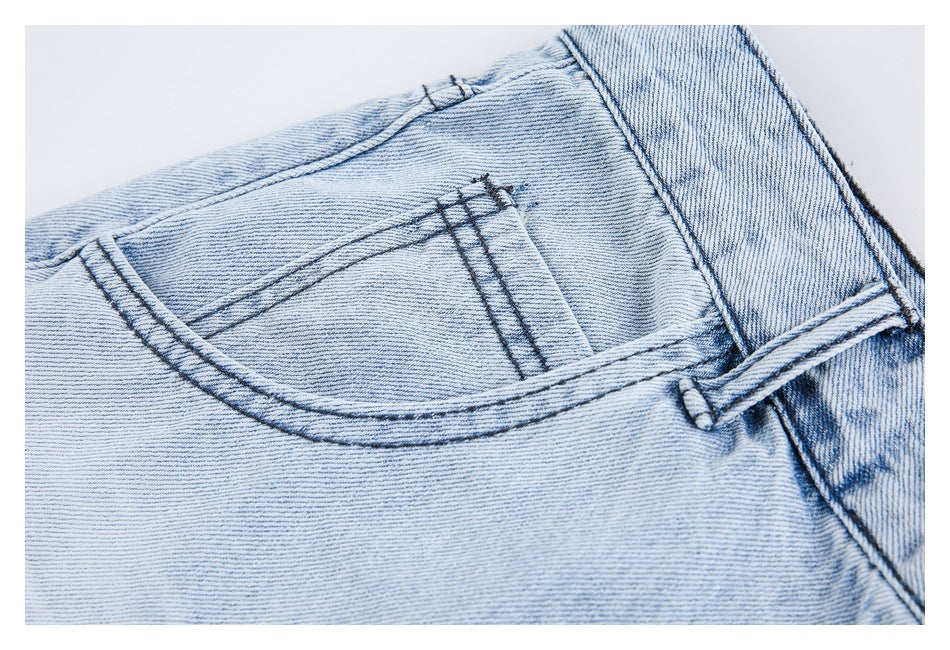 Close-up of a stitched back pocket and waistband on light-wash denim jeans.