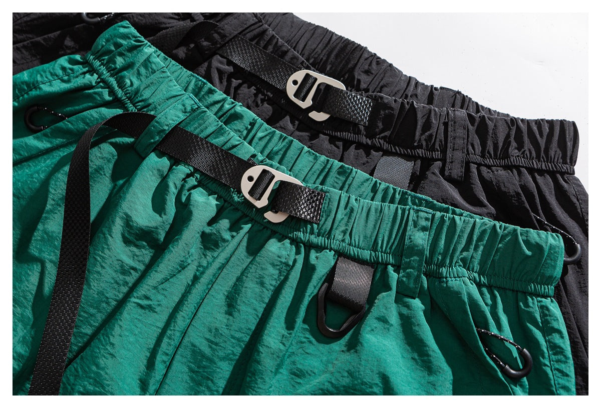 Close-up of teal and black shorts with elastic waistbands, black webbing straps, buckles and loops.