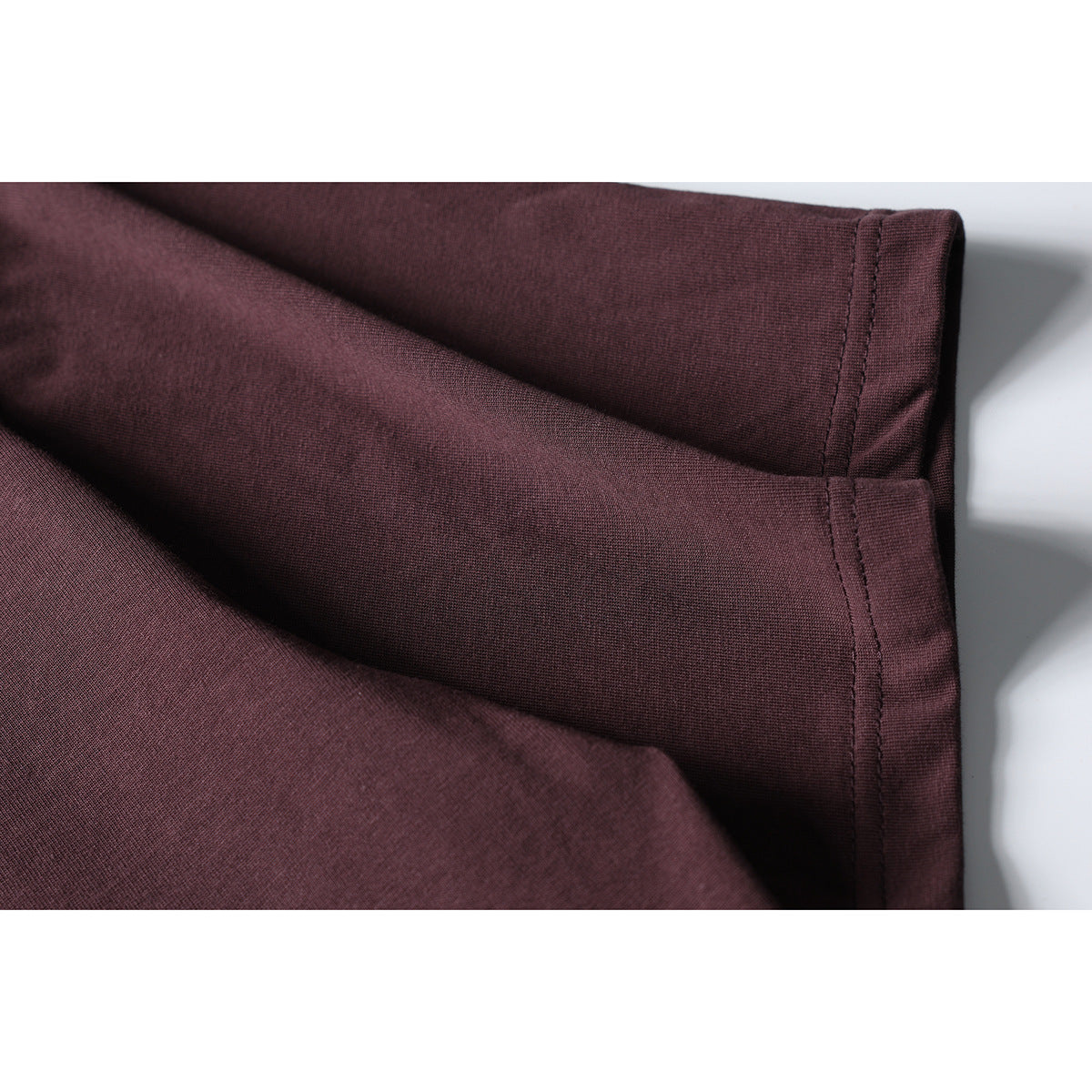 Close-up of a burgundy T-shirt sleeve edge and stitched seam against a white background.