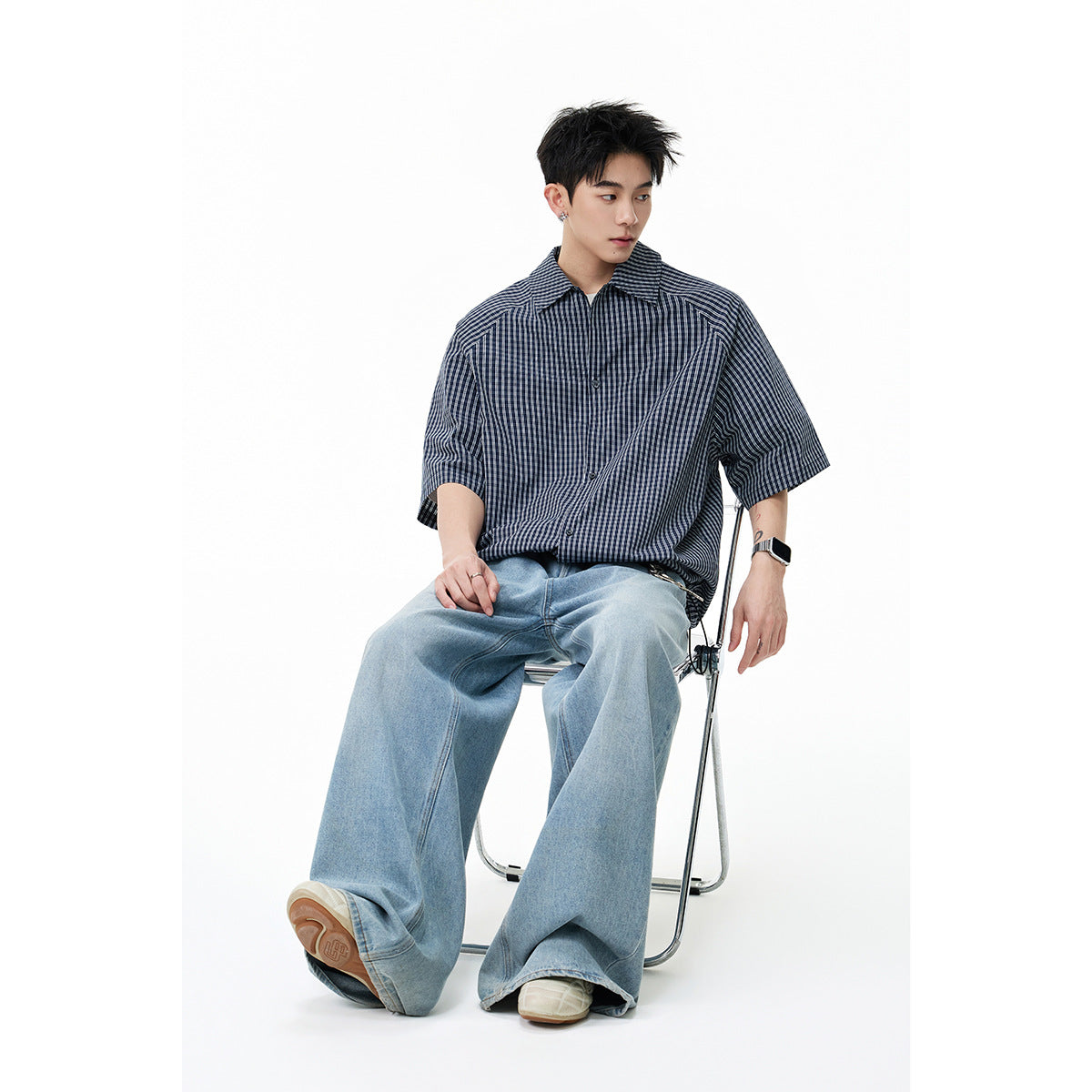Seated model wearing a navy-and-gray checked short-sleeve shirt with light blue wide-leg jeans.