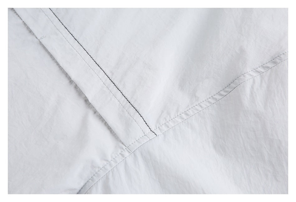 Close-up of intersecting seams on softly creased light gray fabric.