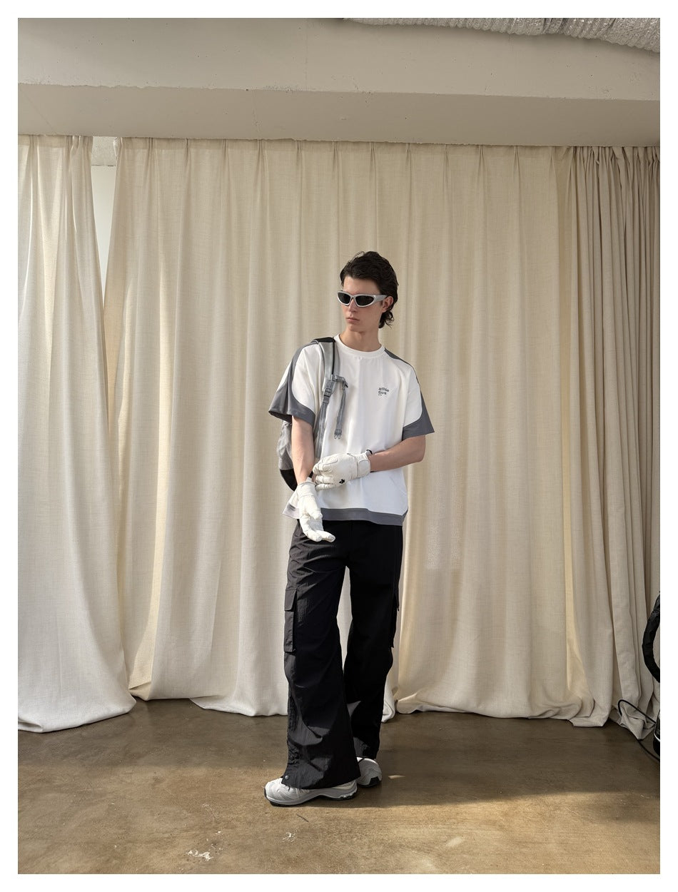 Model wearing a white T-shirt with dark gray shoulder panels, sleeves, and hem, with black cargo pants.