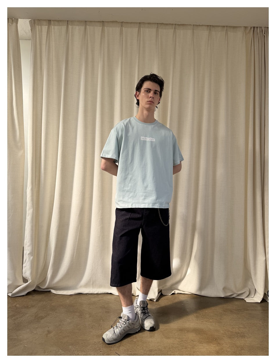 Full-length model wearing a pale blue T-shirt with a small chest print and black shorts.