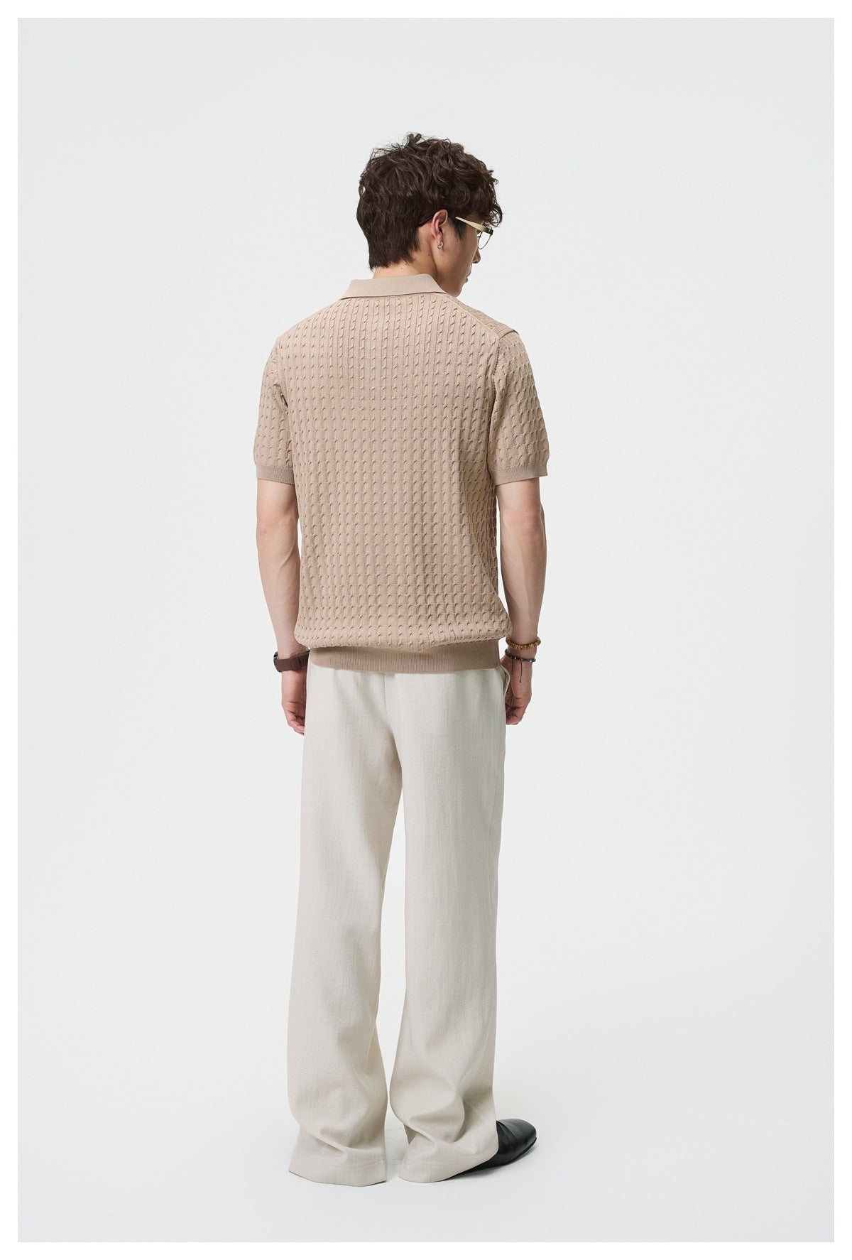 Back view of a man wearing beige wide-leg trousers with a tan textured knit polo and black shoes
