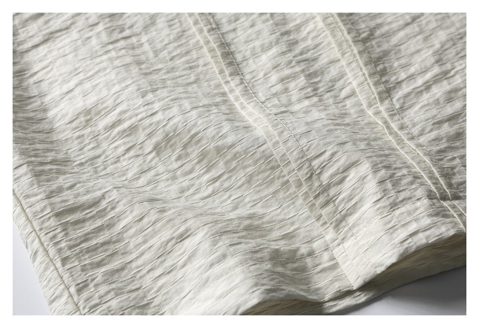 Close-up of pale ivory crinkled fabric with stitched vertical panels and a folded hem.