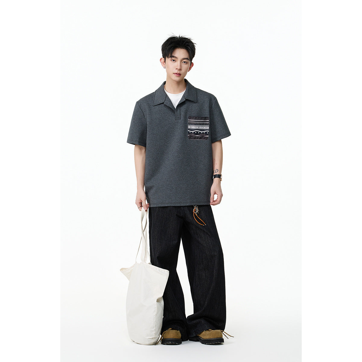 Model wearing a dark charcoal short-sleeve collared polo with a patterned chest pocket and dark wide-leg jeans.