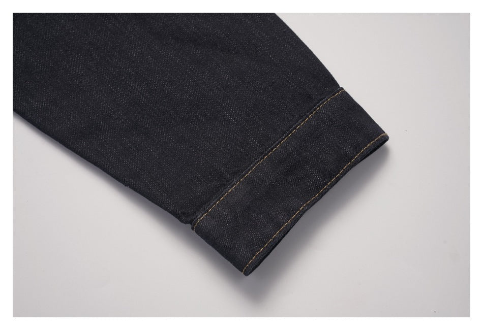 Close-up of a dark denim jacket sleeve ending in a folded cuff with contrast stitching.