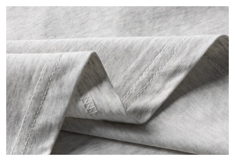 Close-up of the double-stitched hem on light heather-gray T-shirt fabric.