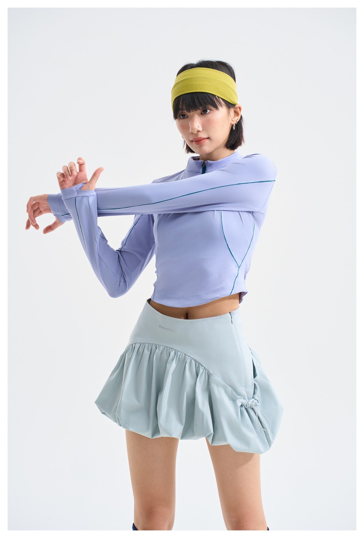 Model stretches in a lilac quarter-zip top with teal piping and a pale blue gathered skirt.