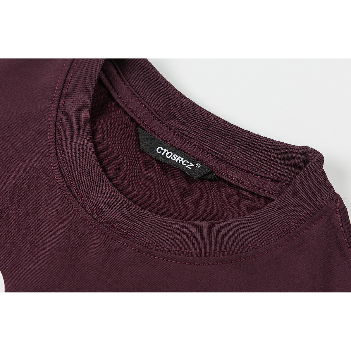 Close-up of the burgundy T-shirt's ribbed crew neckline, stitching, and inner brand label.