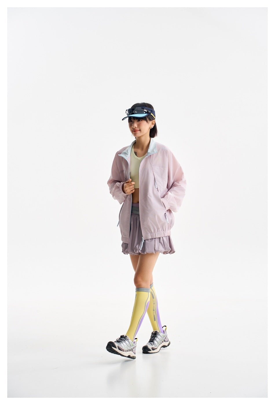 Model wearing a pale pink zip-up jacket with a light blue collar, layered over a top and pleated skirt.