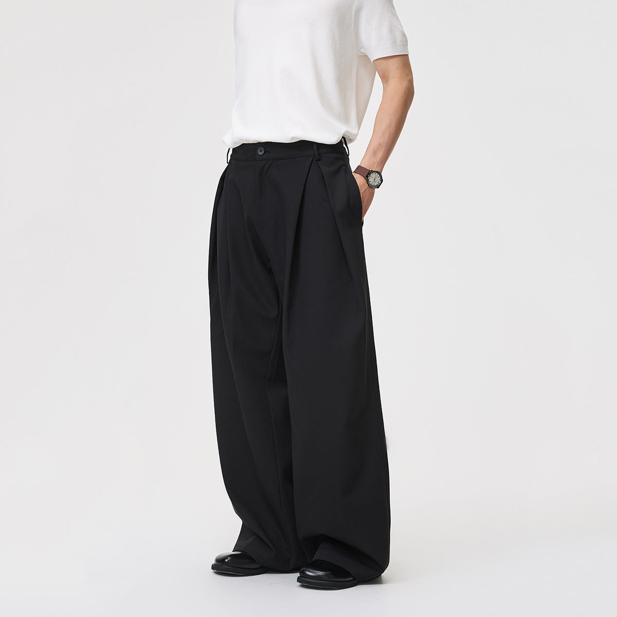 Model wearing black wide-leg trousers, shown from a front three-quarter angle with a hand in the pocket.