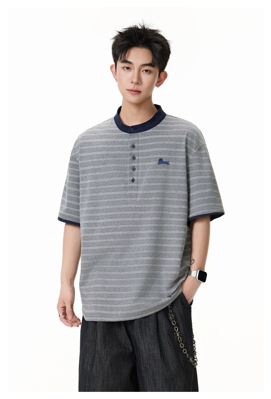 Model wearing a gray fine-striped short-sleeve henley with navy collar and sleeve trim, and dark wide-leg trousers.