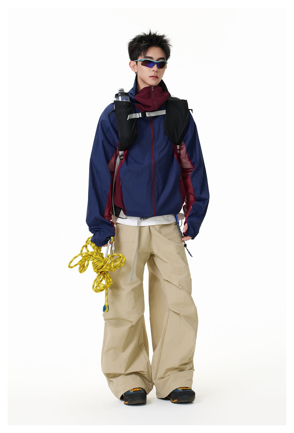 Full-length model wearing a navy hooded jacket with burgundy panels and loose beige trousers.