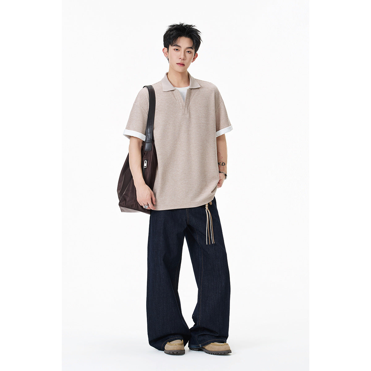 Model wearing a beige short-sleeve polo with white sleeve cuffs, styled with dark wide-leg jeans.