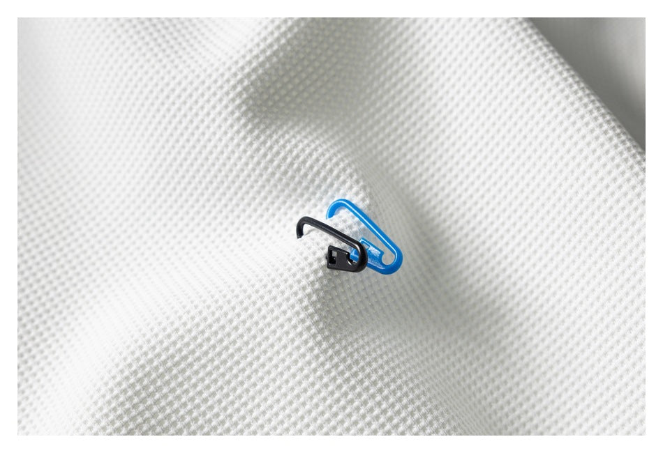 Close-up of white textured fabric with small black and blue plastic clips attached.
