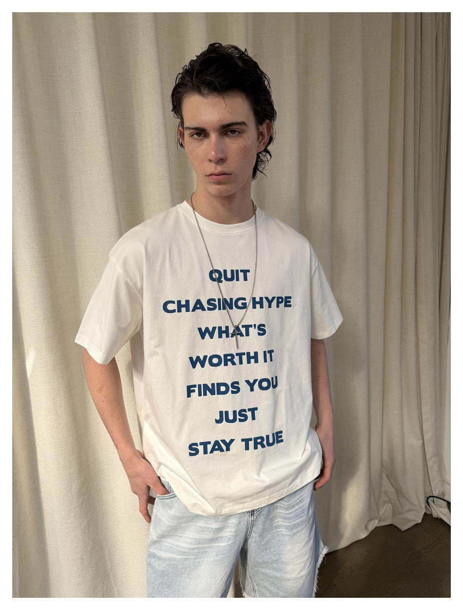 Model wearing a white oversized T-shirt with bold navy text and pale denim shorts, shown from the front.
