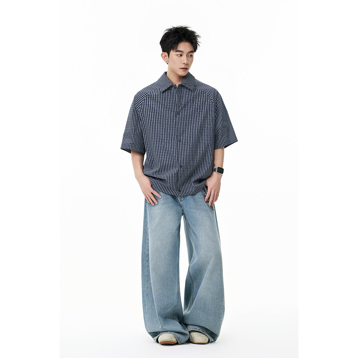 Standing model wearing a navy-and-gray checked short-sleeve button-up shirt with light blue wide-leg jeans.