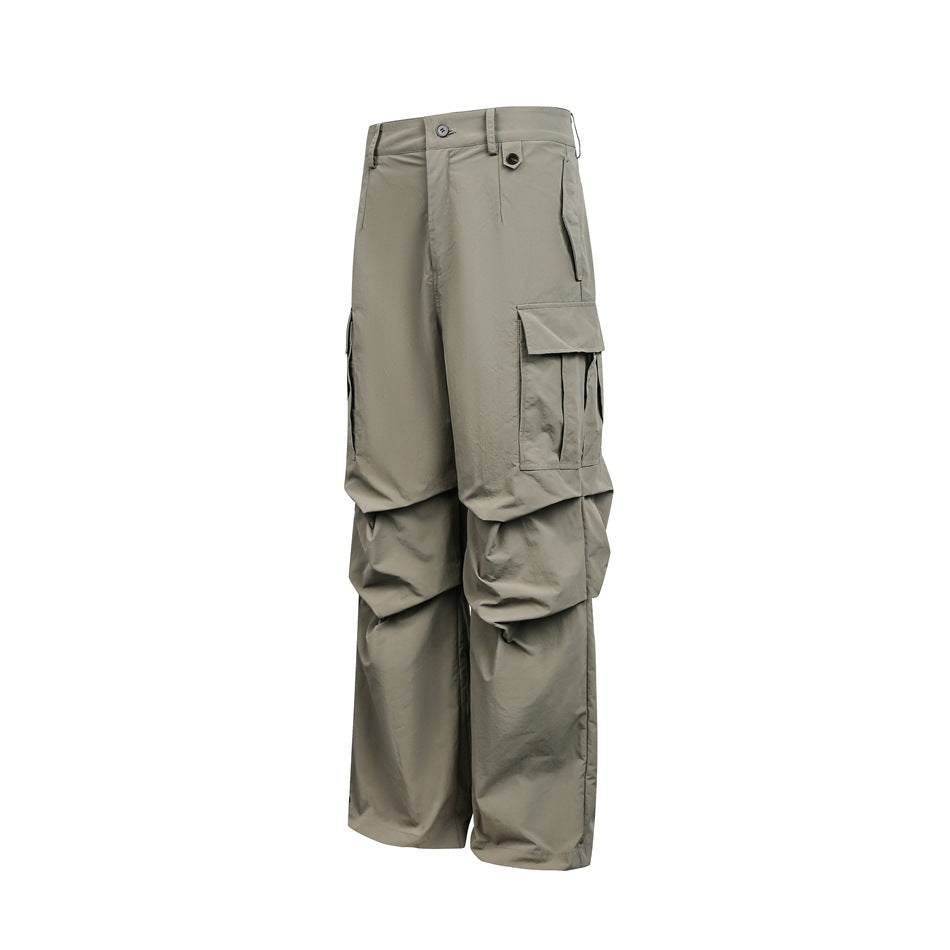 Front view of loose gray-olive cargo pants with wide legs, button closure, and large flap thigh pockets on white.