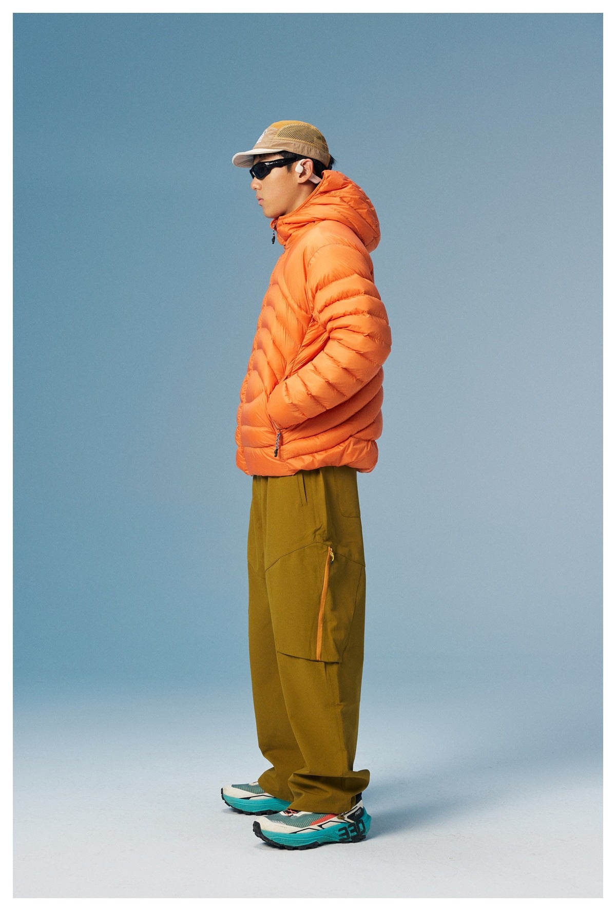 Side view of a model wearing an orange hooded puffer jacket and olive cargo pants.