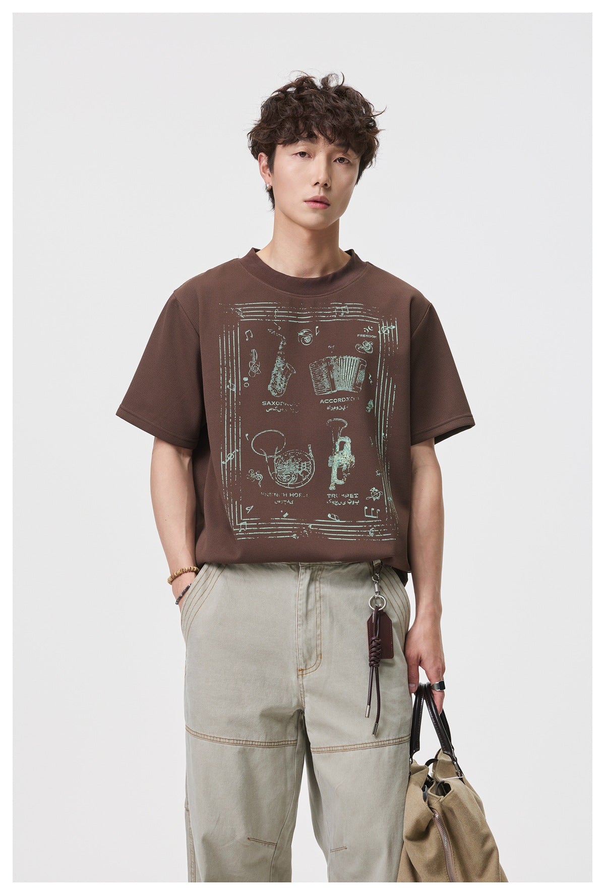 Front view of a model wearing a brown short-sleeve T-shirt with a pale vintage instrument graphic.