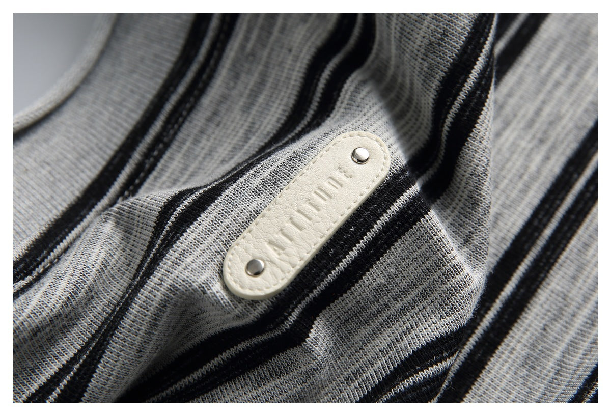 Close-up of a cream-colored embossed patch with metal studs on gray-and-black striped knit fabric.