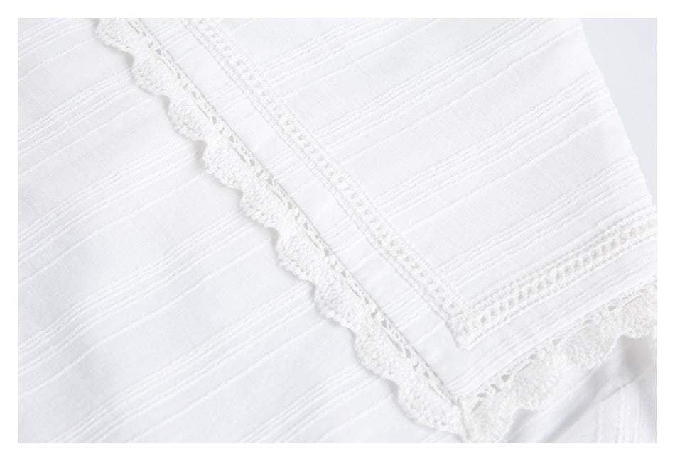 Close-up of white fabric with raised stripe texture and scalloped lace trim along a seam.