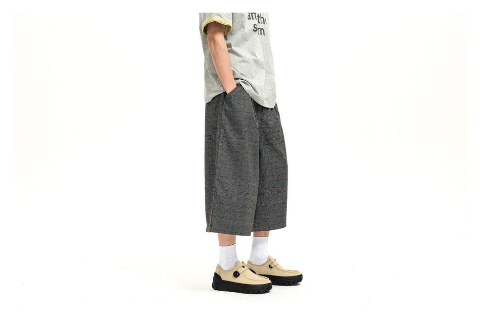 Cropped side view of a model wearing charcoal plaid wide-leg shorts with a gray T-shirt and beige shoes.