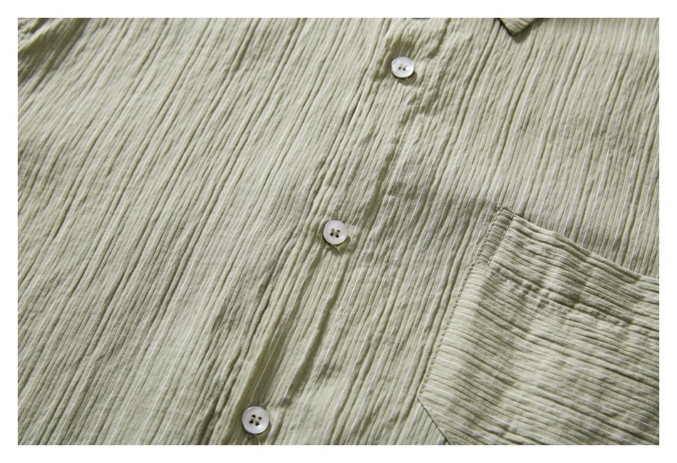 Close-up of an olive-gray shirt’s striped front, white buttons, and chest pocket edge.