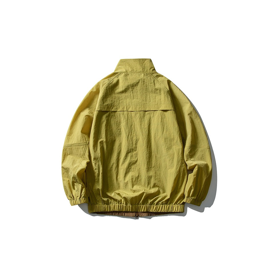 Back view of a mustard yellow-green jacket laid flat, with a stand collar, back yoke, elastic cuffs and hem.