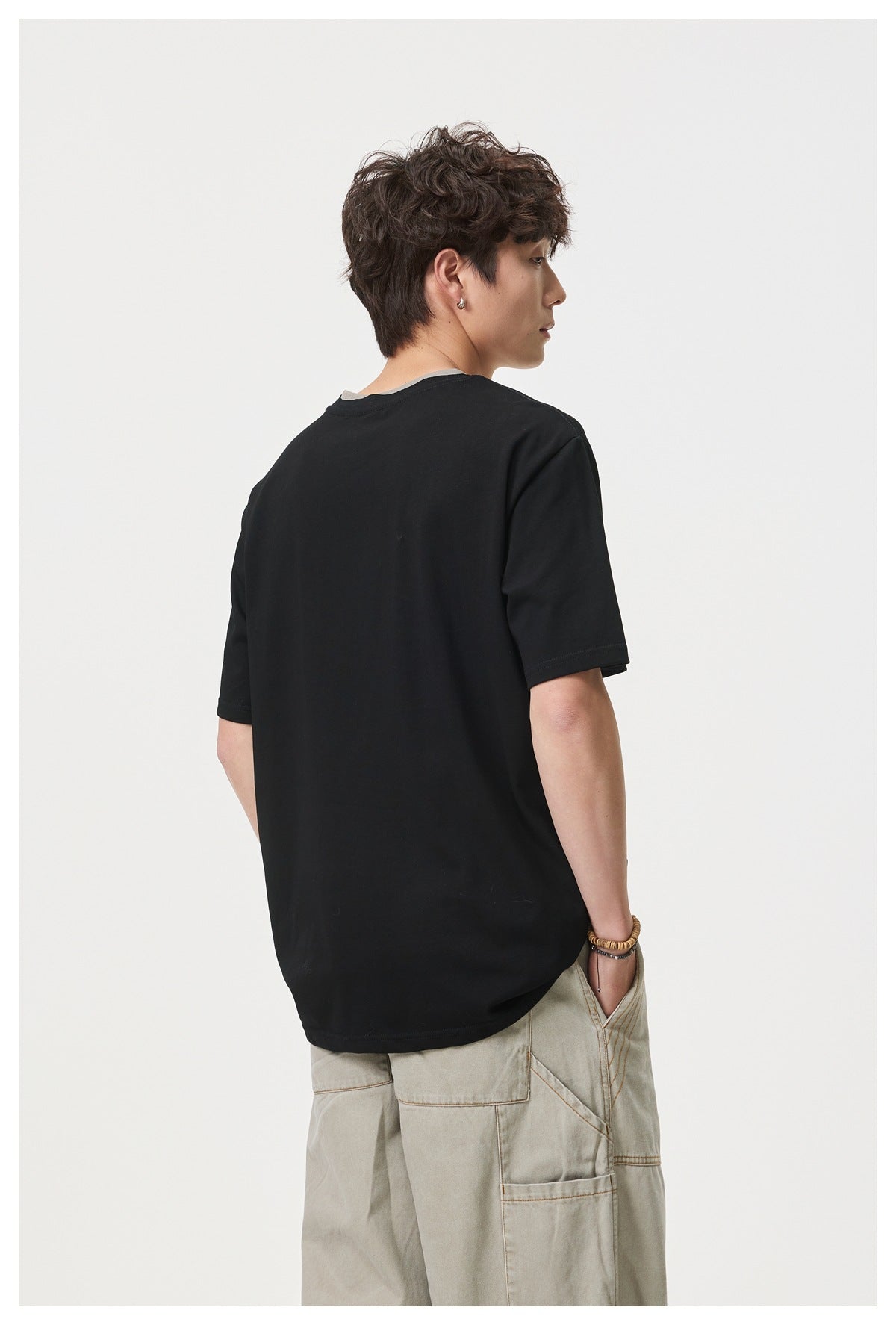 Rear view of a model wearing a plain black short-sleeve T-shirt with beige cargo trousers.