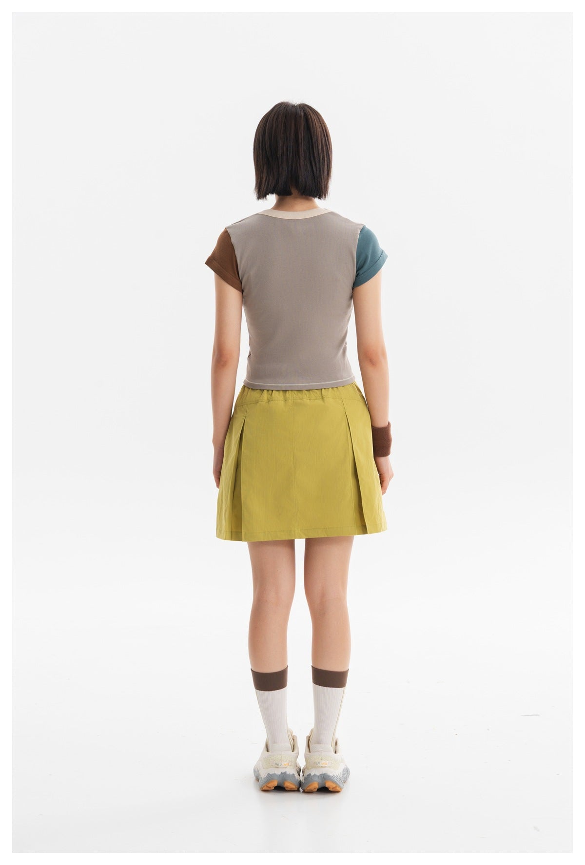 Back view of a model wearing a taupe top with brown and teal sleeves and a mustard skirt.