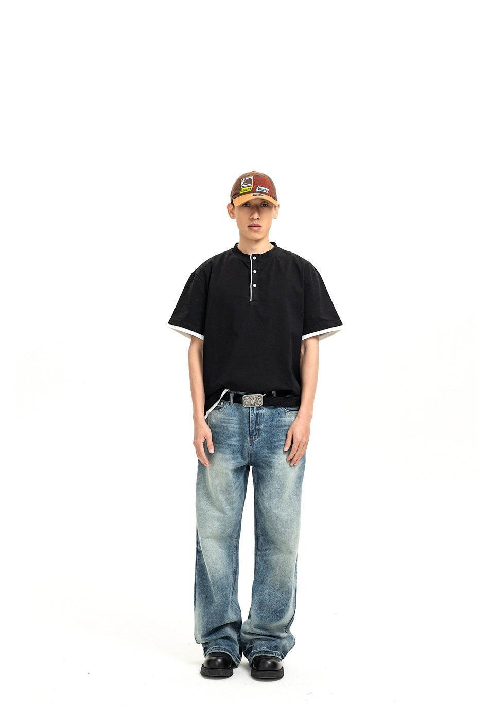 Front view of a model wearing a black short-sleeve henley with white trim and loose blue jeans.