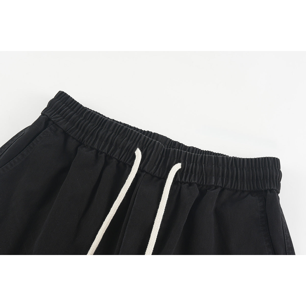 Close-up of black shorts with an elastic waistband and two off-white drawstrings.