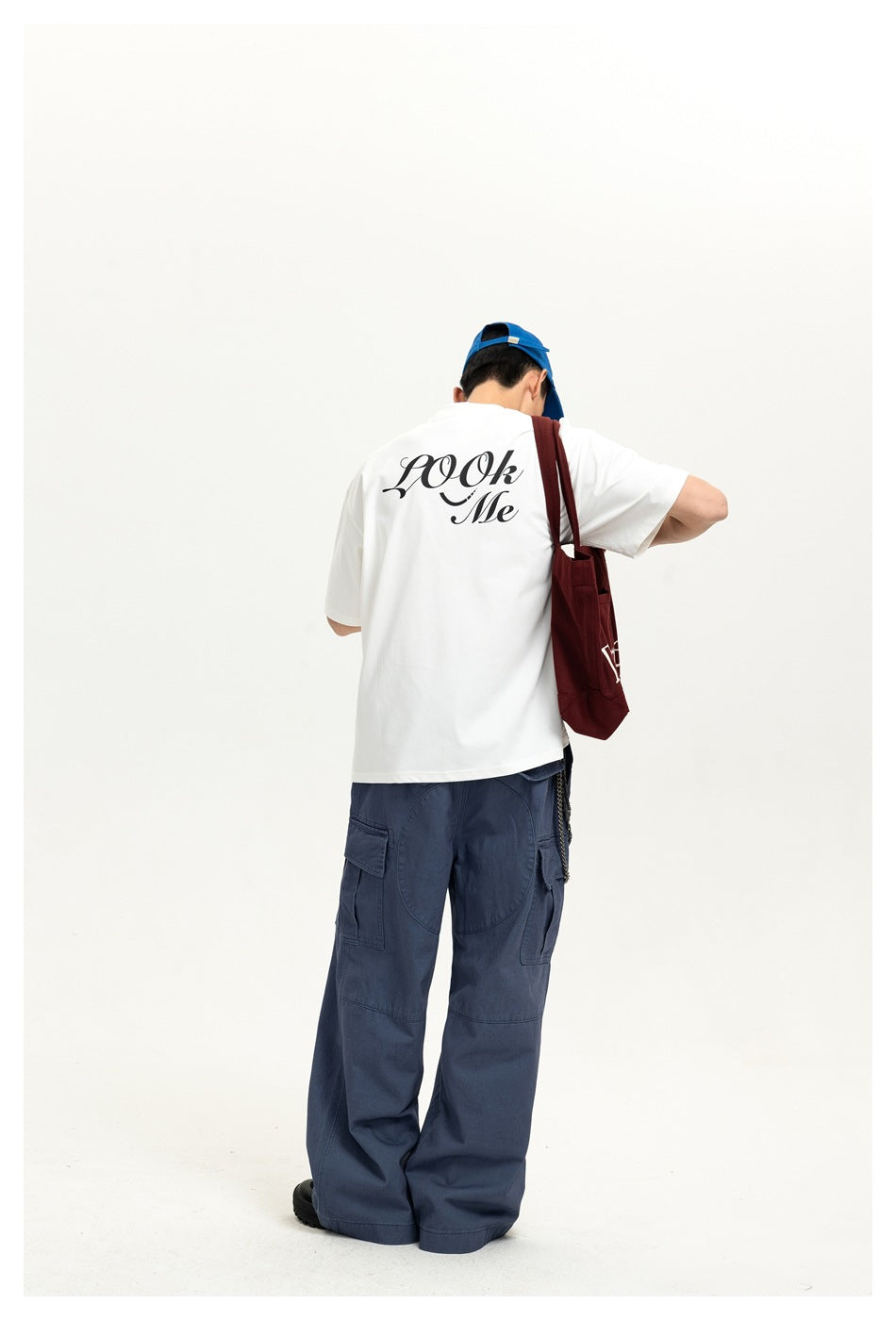 Back view of a model wearing a white T-shirt with large black script lettering and loose blue cargo trousers.