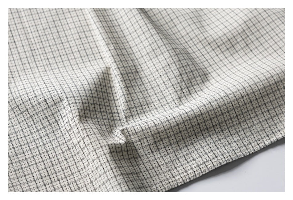 Close-up of cream fabric with a fine black windowpane check, draped to show its surface.