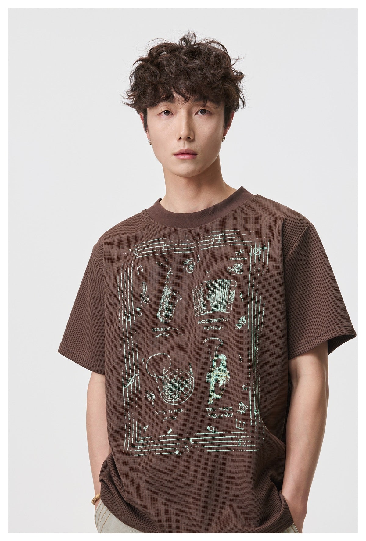 Model wearing a brown short-sleeve T-shirt with a pale mint illustrated graphic on the front.