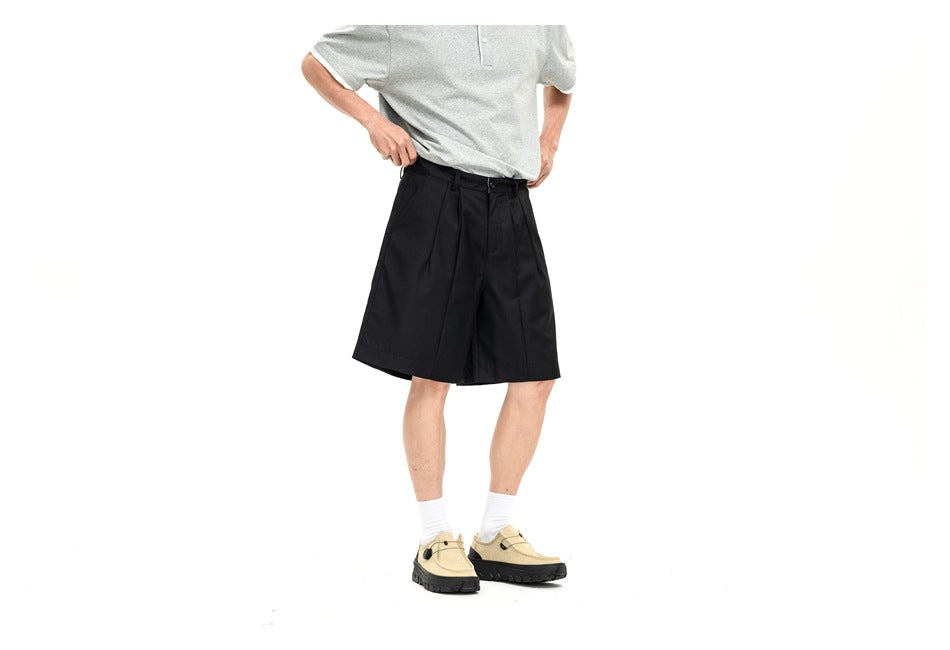 Cropped view of a model wearing black pleated shorts with a light gray short-sleeve shirt.