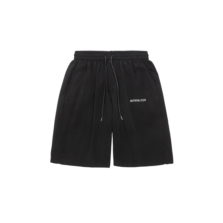 Black knee-length shorts with elastic drawstring waist, side pockets and small white embroidered text, front flat lay