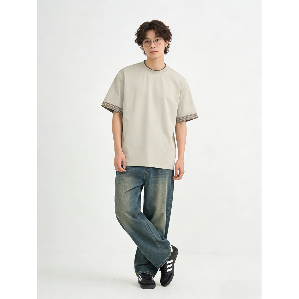 Model wearing a light beige crew-neck T-shirt with checked sleeve cuffs and loose blue jeans.