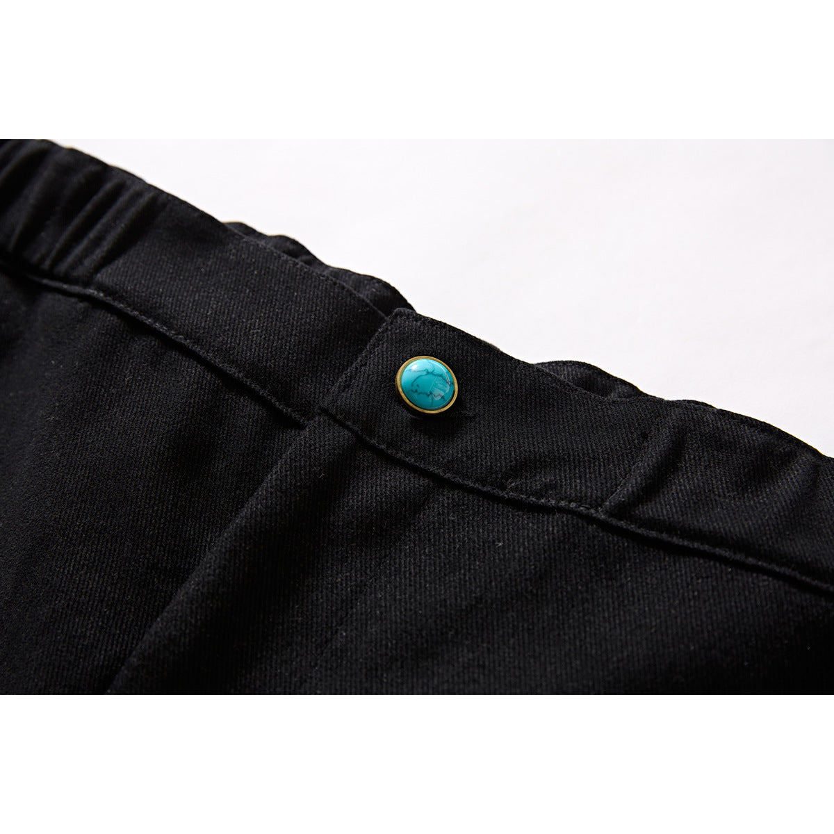 Close-up of black shorts waistband with a turquoise button and visible stitching.