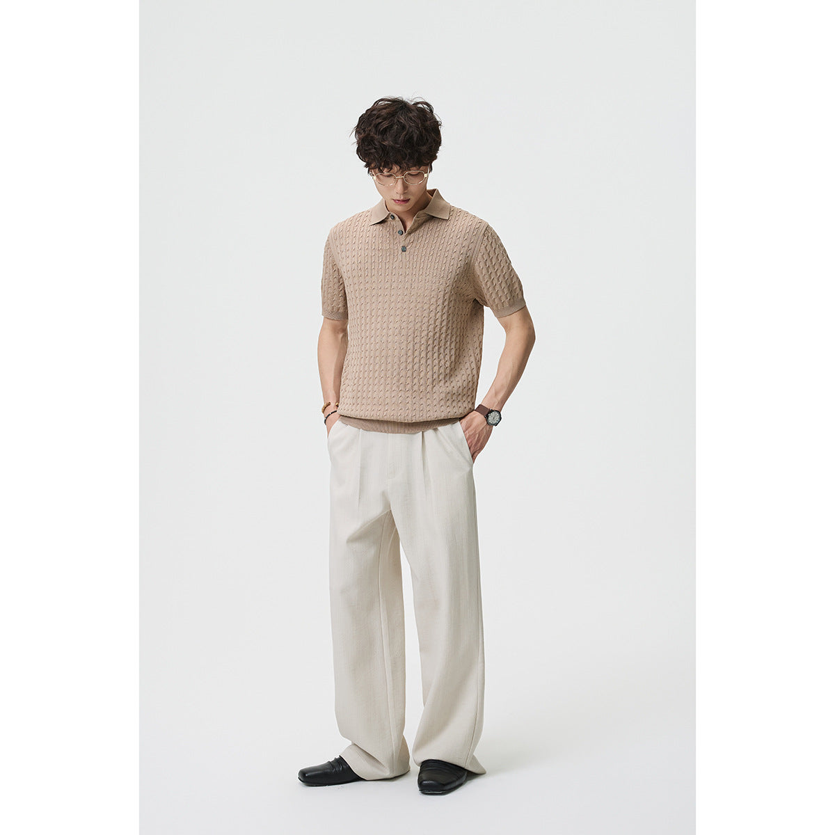 Model wearing a taupe textured short-sleeve polo and loose ivory trousers, shown from the front.