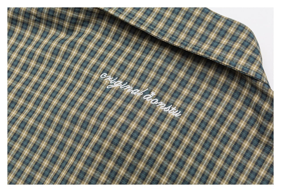 Close-up of white embroidered lettering below the collar of a blue, tan, and cream plaid shirt.