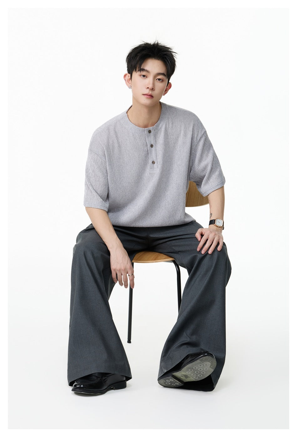 Seated model wearing a light gray short-sleeve henley shirt with dark wide-leg trousers.