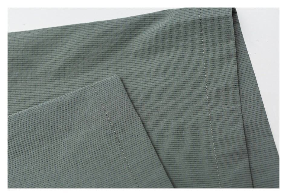 Close-up of stitched seams and overlapping panels on muted gray-green ribbed fabric.