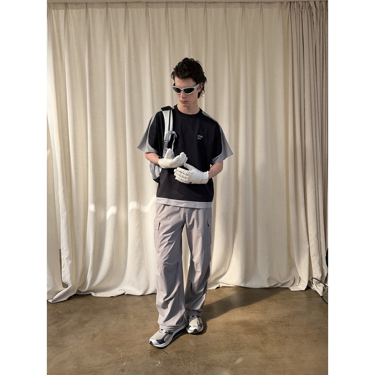 Model wearing a black T-shirt with gray sleeves and hem, loose gray cargo pants, and white gloves.