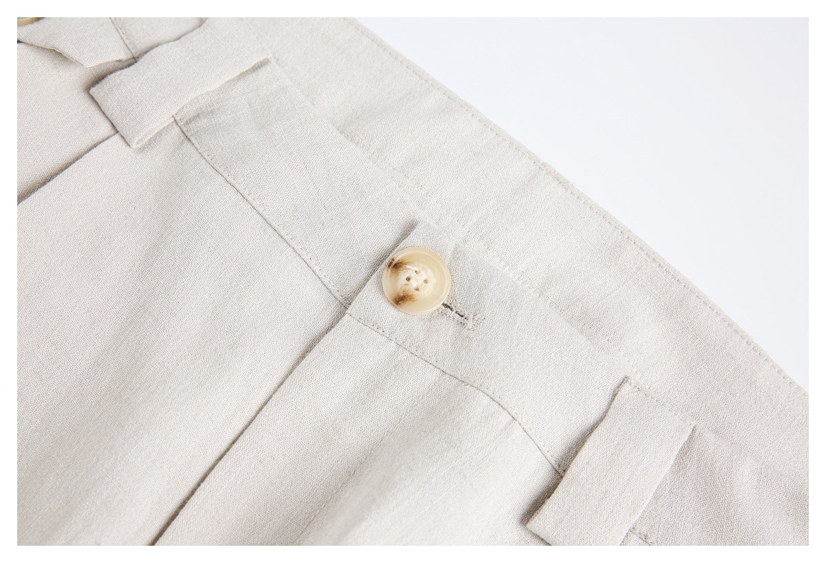 Close-up of ivory trouser waistband with a tan button and belt loops.