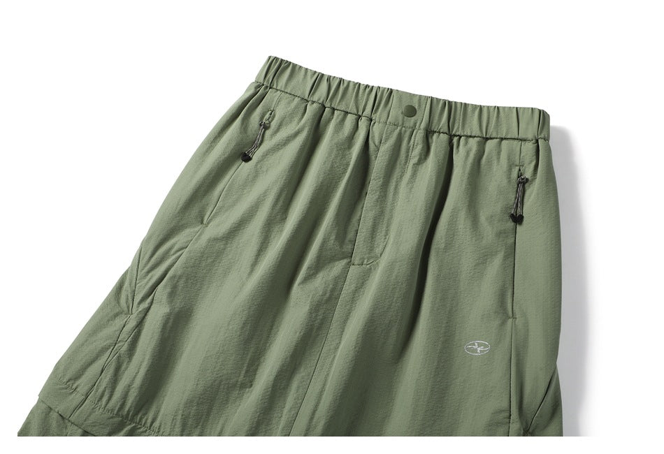 Sage green skirt front shown flat, with an elastic waistband, snap closure, zip pockets and a small logo.