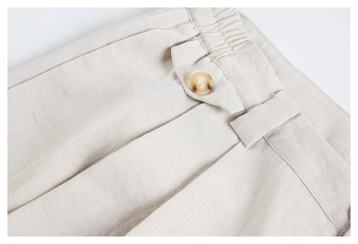 Close-up of light beige trousers showing the waistband, button, belt loop, and front pleats.