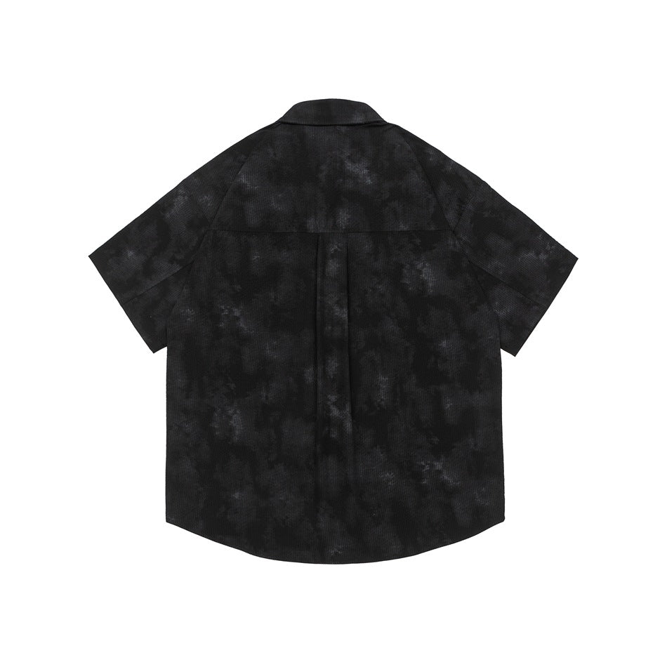 Back view of a black short-sleeve button-up shirt with a mottled pattern and a center pleat.